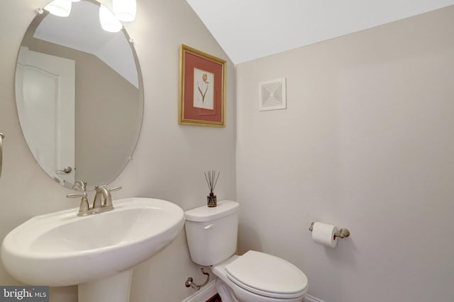 half bathroom featuring a sink, baseboards, toilet, and vaulted ceiling