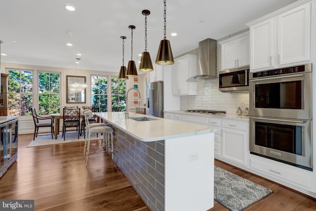 kitchen with tasteful backsplash, a sink, wall chimney range hood, appliances with stainless steel finishes, and dark wood-style flooring