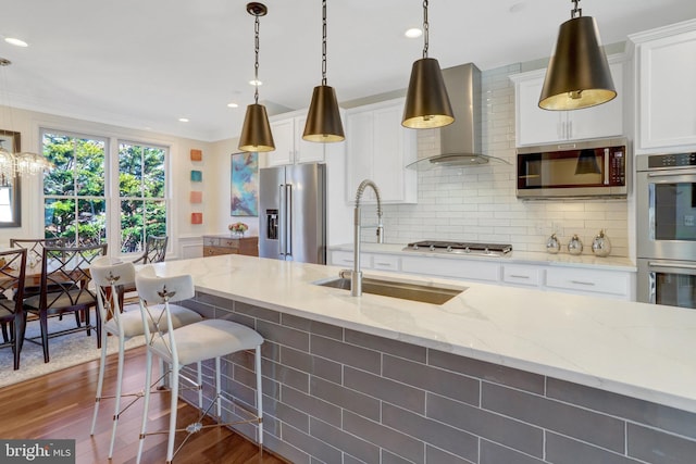 kitchen with a sink, ornamental molding, dark wood-type flooring, stainless steel appliances, and wall chimney exhaust hood