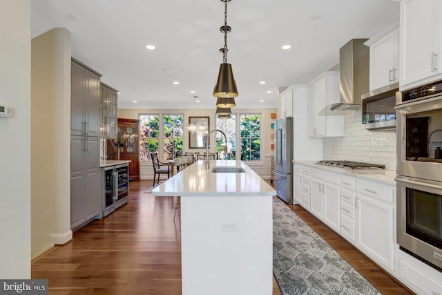 kitchen with a sink, wall chimney exhaust hood, appliances with stainless steel finishes, and dark wood-style floors