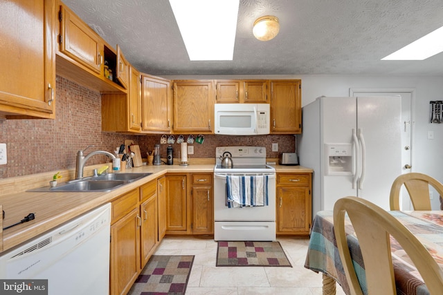 kitchen featuring white appliances, a skylight, a sink, light countertops, and tasteful backsplash