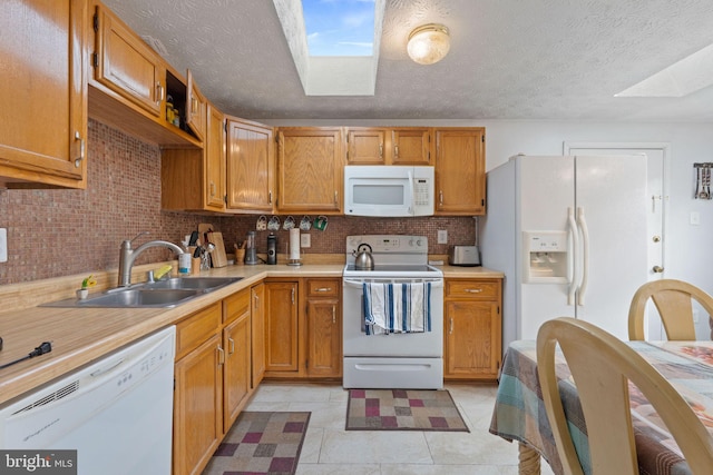 kitchen with white appliances, tasteful backsplash, a skylight, light countertops, and a sink