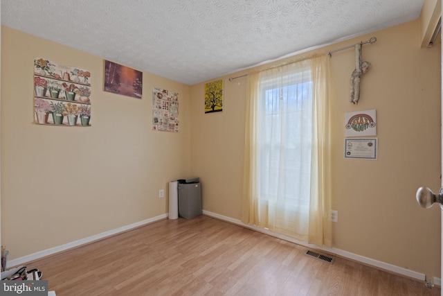 unfurnished room featuring a textured ceiling, light wood-type flooring, visible vents, and baseboards