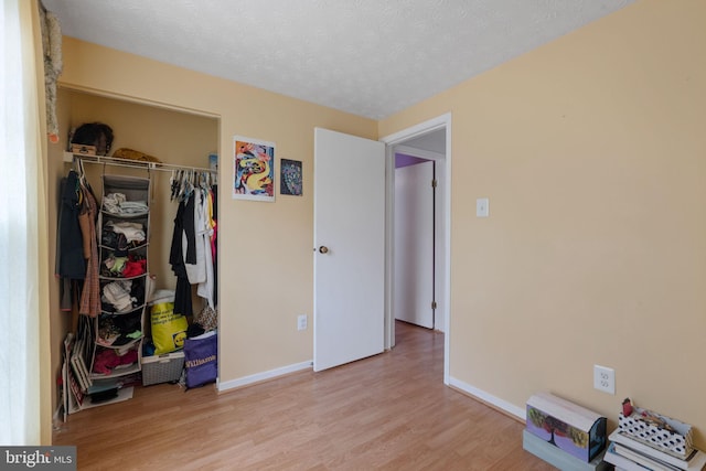 bedroom featuring a textured ceiling, a closet, light wood-style flooring, and baseboards