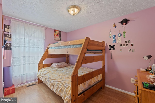 bedroom with visible vents, a textured ceiling, baseboards, and wood finished floors