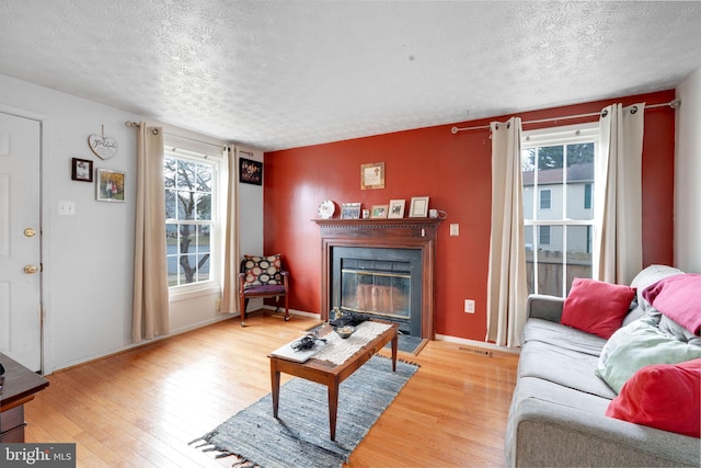 living area with light wood-style floors, a glass covered fireplace, a textured ceiling, and baseboards