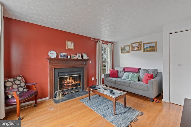 living area featuring a glass covered fireplace, a textured ceiling, baseboards, and wood finished floors