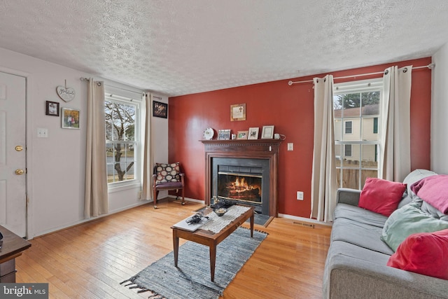 living area featuring a textured ceiling, a lit fireplace, hardwood / wood-style flooring, and baseboards