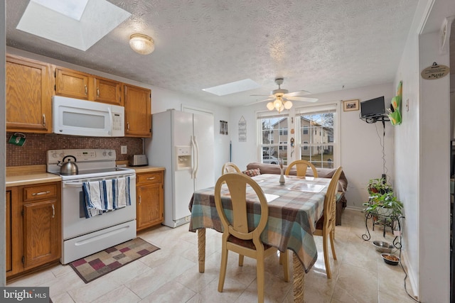 kitchen featuring white appliances, tasteful backsplash, a skylight, brown cabinetry, and light countertops