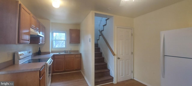 kitchen featuring light countertops, a sink, wood finished floors, white appliances, and under cabinet range hood