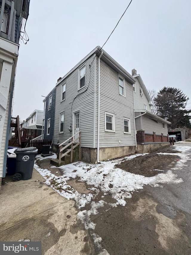 view of snow covered exterior featuring a chimney and central AC unit