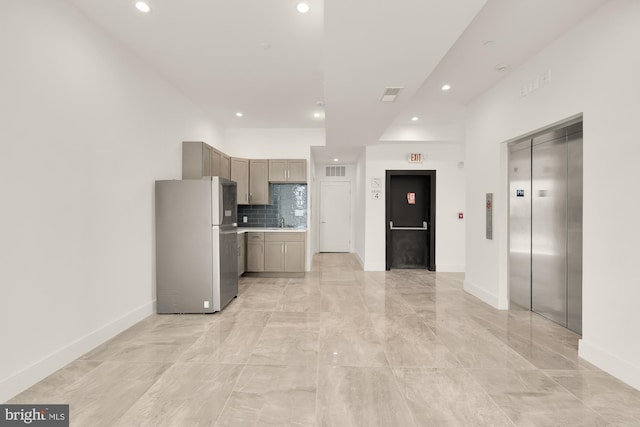 kitchen featuring a sink, backsplash, freestanding refrigerator, elevator, and light countertops