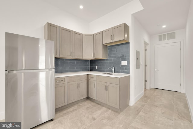 kitchen featuring visible vents, a sink, backsplash, freestanding refrigerator, and light countertops