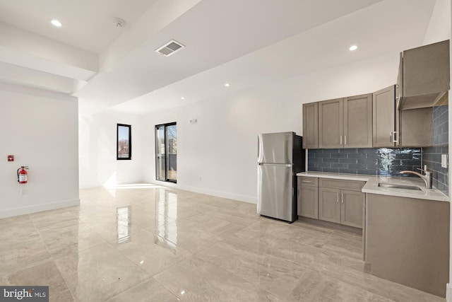 kitchen with a sink, freestanding refrigerator, light countertops, decorative backsplash, and baseboards