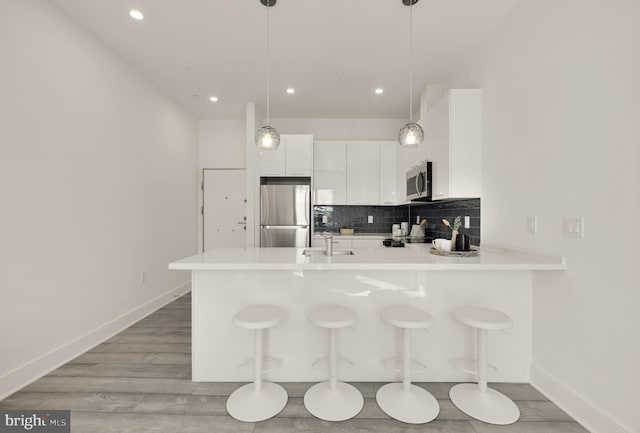 kitchen with backsplash, light countertops, a peninsula, stainless steel appliances, and a sink