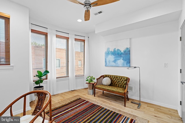 living area featuring baseboards, light wood-type flooring, visible vents, and a ceiling fan