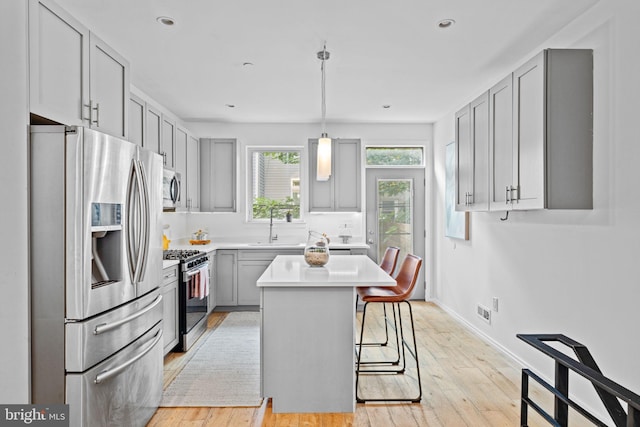 kitchen featuring gray cabinetry, a sink, a kitchen breakfast bar, light countertops, and appliances with stainless steel finishes