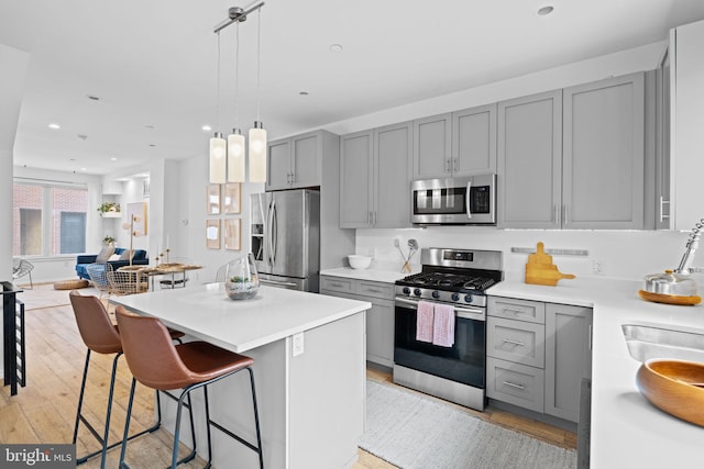 kitchen with stainless steel appliances, light wood-type flooring, gray cabinets, and a kitchen bar