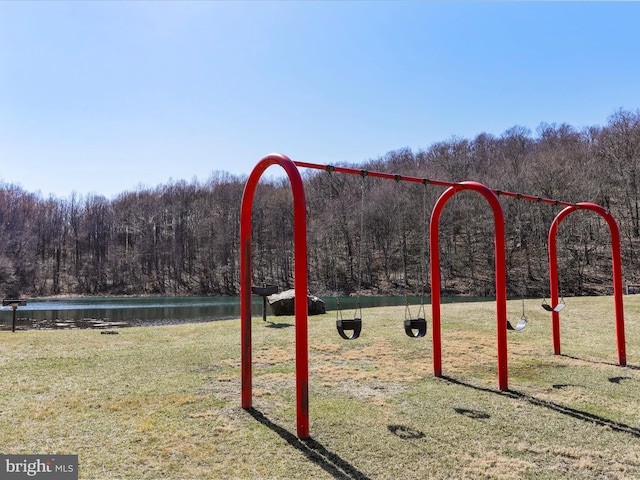 view of playground featuring a lawn, a forest view, and a water view