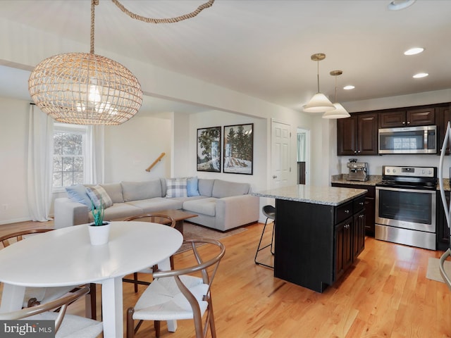 kitchen with a breakfast bar, stainless steel appliances, light wood-style floors, pendant lighting, and open floor plan