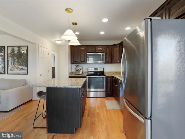 kitchen featuring decorative light fixtures, light wood-style floors, appliances with stainless steel finishes, a breakfast bar area, and dark brown cabinets