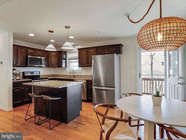 kitchen featuring a kitchen island, a sink, dark brown cabinetry, light wood-style floors, and appliances with stainless steel finishes