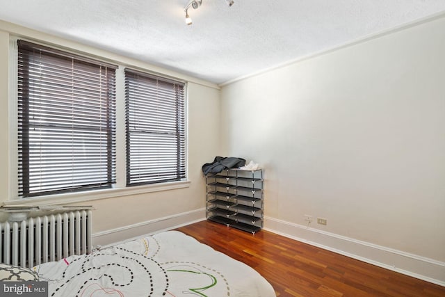 bedroom featuring baseboards, a textured ceiling, radiator heating unit, and wood finished floors