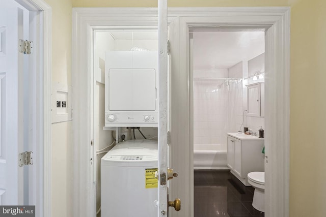 full bath with stacked washing maching and dryer, a sink, toilet, and tile patterned floors