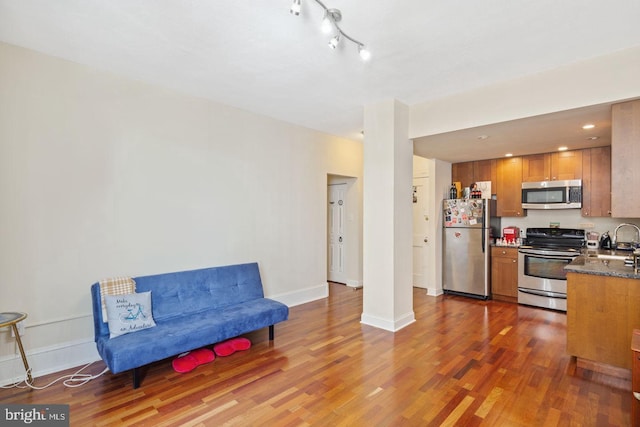 kitchen with stainless steel appliances, a sink, wood finished floors, baseboards, and brown cabinetry