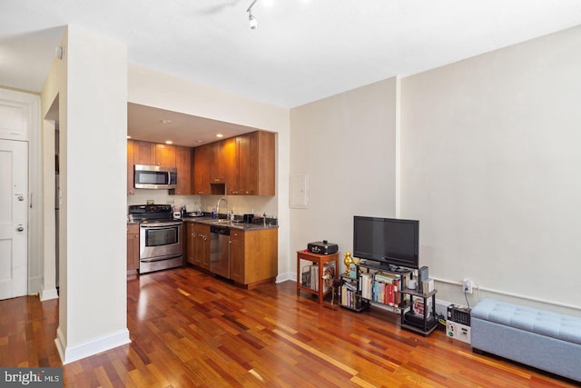 kitchen with dark wood-style floors, brown cabinets, dark countertops, appliances with stainless steel finishes, and a sink