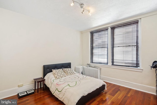 bedroom featuring baseboards, a textured ceiling, wood finished floors, and radiator