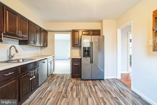 kitchen with light countertops, appliances with stainless steel finishes, dark wood-type flooring, a sink, and dark brown cabinets