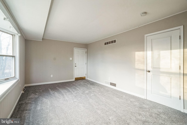 unfurnished room with carpet, visible vents, crown molding, and baseboards