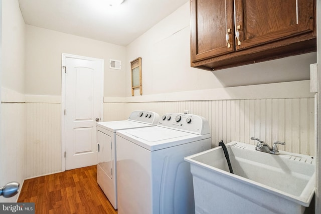 clothes washing area with cabinet space, visible vents, a wainscoted wall, independent washer and dryer, and a sink