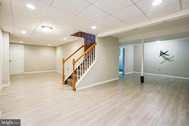 finished below grade area featuring stairs, a drop ceiling, baseboards, and wood finished floors