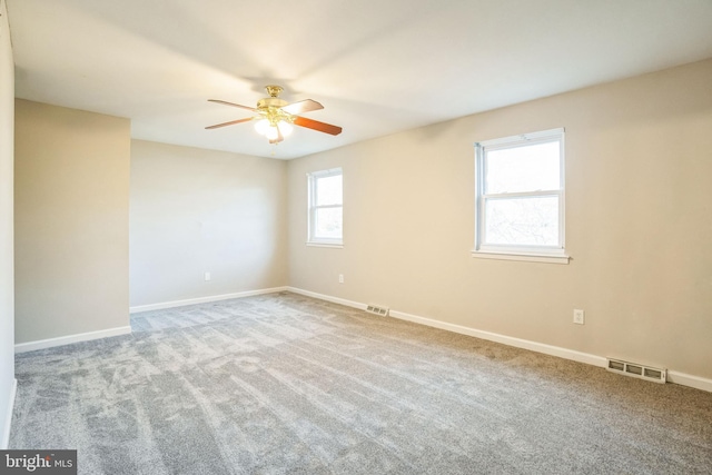 carpeted spare room featuring baseboards, visible vents, and ceiling fan