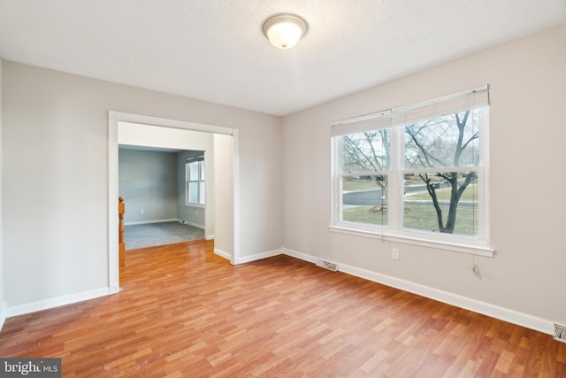 unfurnished room with light wood-type flooring, visible vents, and baseboards