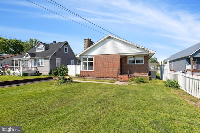 back of house with a yard, brick siding, fence, and a chimney