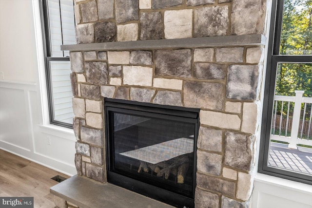 details featuring a stone fireplace, a decorative wall, wood finished floors, visible vents, and wainscoting