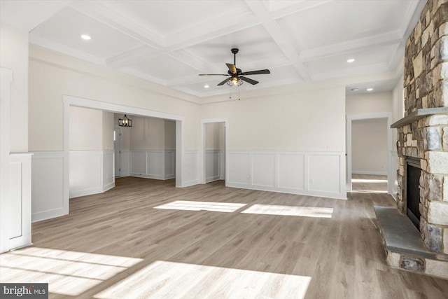 unfurnished living room with light wood-style flooring, ceiling fan, beamed ceiling, and a stone fireplace