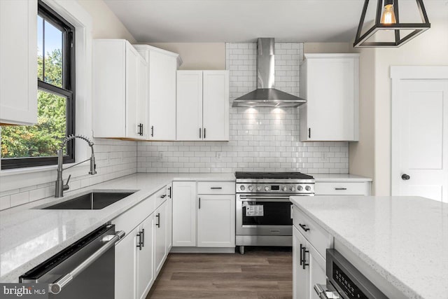 kitchen with light stone counters, a sink, wall chimney range hood, appliances with stainless steel finishes, and decorative backsplash