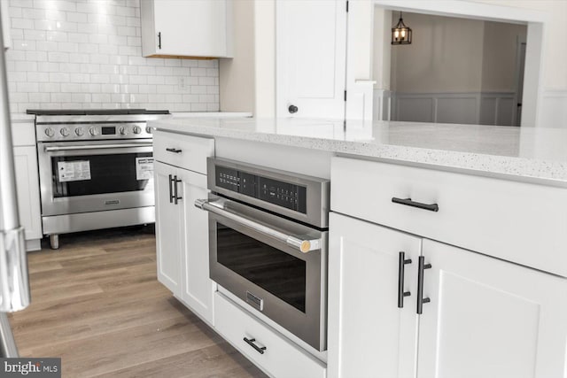 kitchen featuring white cabinets, light wood-style floors, stainless steel appliances, and decorative backsplash