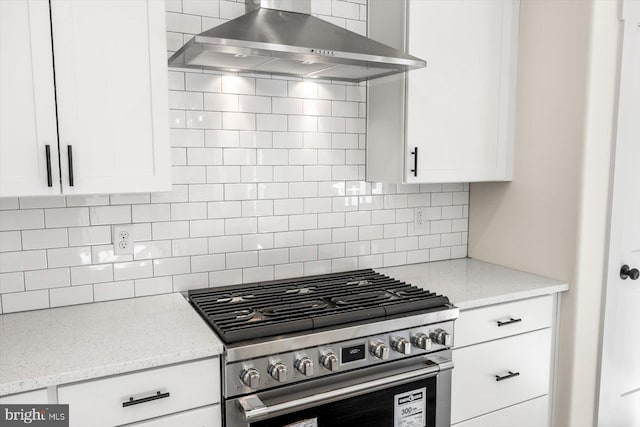 kitchen with tasteful backsplash, white cabinetry, light stone countertops, stainless steel gas range oven, and wall chimney exhaust hood