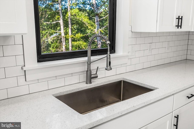 interior details featuring white cabinets, a sink, backsplash, and light stone countertops