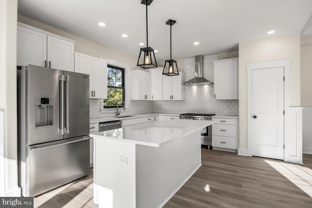 kitchen with light countertops, backsplash, appliances with stainless steel finishes, wood finished floors, and wall chimney exhaust hood