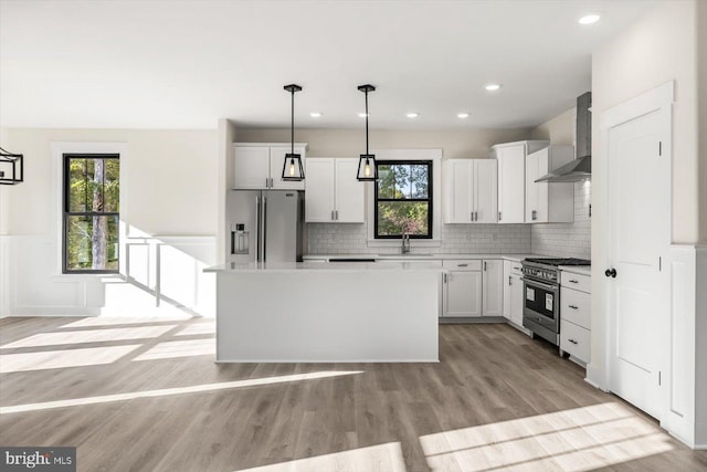 kitchen with stainless steel appliances, a sink, white cabinets, wall chimney exhaust hood, and light wood finished floors