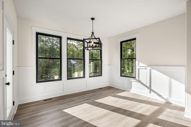 unfurnished dining area featuring visible vents, a decorative wall, an inviting chandelier, wainscoting, and wood finished floors