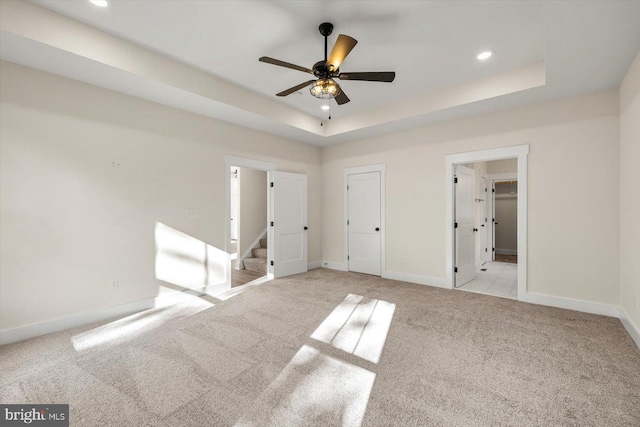 unfurnished bedroom featuring baseboards, a tray ceiling, and light colored carpet