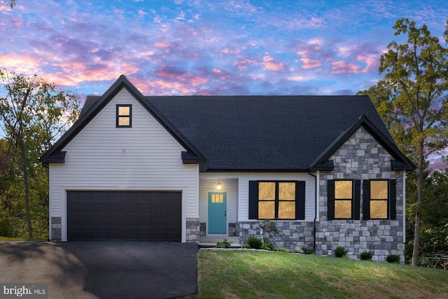 view of front of house with a shingled roof, a lawn, a garage, stone siding, and driveway