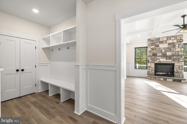 mudroom featuring ceiling fan, a stone fireplace, a decorative wall, a wainscoted wall, and wood finished floors